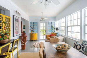 A spacious room with a dining table, chairs, a sofa, and a large window with blinds.