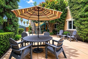 A patio with a round table and chairs, an umbrella, and a staircase leading to a building. - Sunset Cliffs Escape | Steps to Ocean Beach & Pier (San Diego)