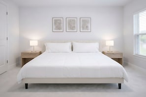 Ein Schlafzimmer mit einem großen Bett, zwei Nachttischen mit Lampen und drei gerahmten Kunstwerken an der Wand.
