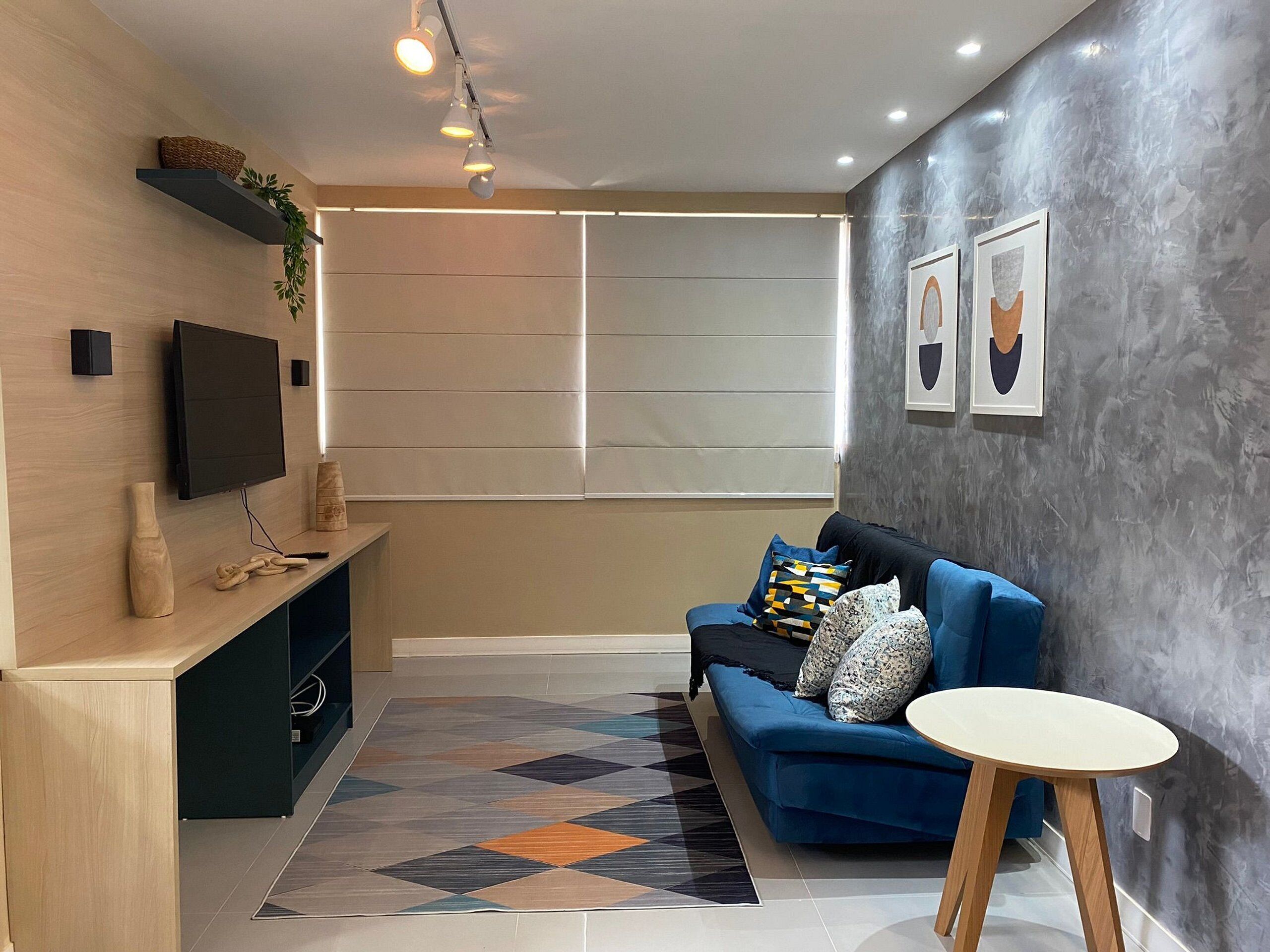 A modern living room with a blue sofa, a small round table, a flat-screen TV, a wooden console, and a patterned rug.