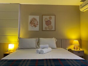 Ein Hotelzimmer mit einem Bett, zwei Nachttischlampen, einem Nachttisch mit Lampe und zwei an der Wand hängenden Kunstwerken.