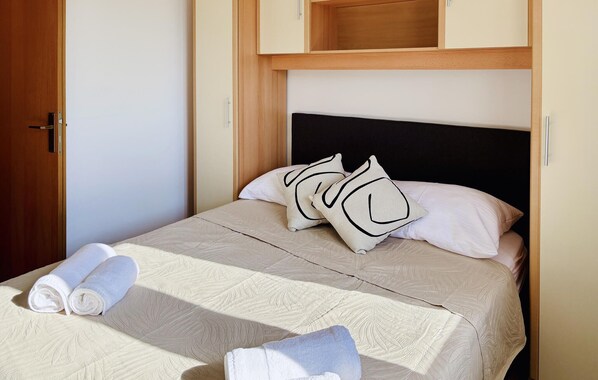 Ein ordentlich bezogenes Bett mit einer gemusterten Tagesdecke, zwei aufgerollten Handtüchern und zwei Zierkissen.