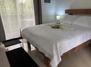 A neatly made bed with a white bedspread, a wooden headboard, and a bedside lamp. - 🌿 Private Getaway in La Fortuna -Bungalows Jacuzzi, River and Nature ✨ 20 min. (Fortuna)