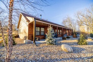 A log cabin with a porch, a small deck, and a gravel driveway. - Luxe Country Lodge | Fire Pit & Acreage (McLouth)