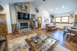 A spacious living area with a stone fireplace, wooden furniture, and deer antlers on the walls. - Luxe Country Lodge | Fire Pit & Acreage (McLouth)