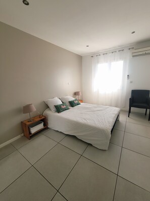 A bedroom with a bed, nightstands, a chair, and a window with curtains. - 🌿 Villa L'Olivier Private pool, garden, 8 people, air conditioning and beaches 4 km away 🌊 (Portiragnes)