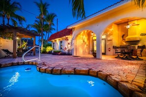 A swimming pool with a built-in slide, a covered patio area with outdoor furniture, and a well-lit entrance. - Waterfront Pool Home w/ Private Dock, Tiki Hut & Backyard Oasis (Marathon)