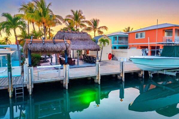 A marina with a thatched-roof structure, a dock, a boat, and a building with a balcony. - Waterfront Pool Home w/ Private Dock, Tiki Hut & Backyard Oasis (Marathon)