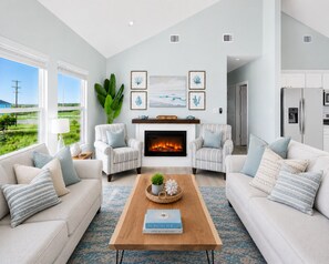 A living room with a fireplace, two armchairs, a sofa, a coffee table with a book, and a view of the outdoors. - Beachfront Hot Tub overlooking gulf, Bar & Games, Pet-Friendly (Gilchrist,)