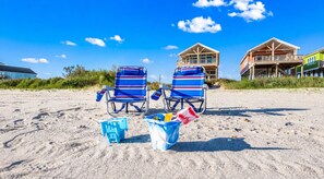 Two beach chairs with striped blue and red fabric, two blue and one white bucket with items, and two beach houses in the background. - Beachfront Hot Tub overlooking gulf, Bar & Games, Pet-Friendly (Gilchrist,)