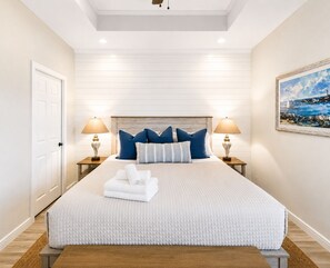 A bedroom with a large bed, two bedside lamps, a painting on the wall, and a door on the left. - Beachfront Hot Tub overlooking gulf, Bar & Games, Pet-Friendly (Gilchrist,)