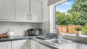 Una cucina moderna con mobili bianchi, un lavello in acciaio inossidabile e una finestra con vista sul verde.