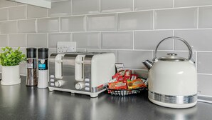 Un piano di lavoro in cucina con un tostapane, un bollitore, contenitori per spezie, una pianta in vaso e un cesto di biscotti.