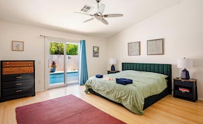 Camera da letto con un letto, una cassettiera, una ventola a soffitto, un comodino, una lampada e vista su una piscina esterna.
