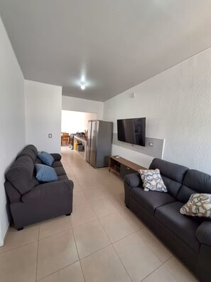 A modern living room with two dark sofas, a flat-screen TV, and a kitchen in the background. - Contemporary House with Pool Access (Sitio del Niño)