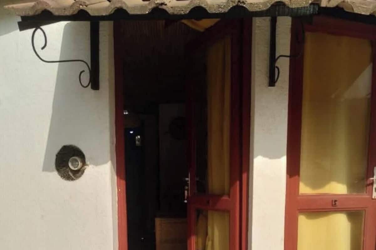 Una entrada de casa con techo de tejas, una puerta con cortinas y un felpudo pequeño en el suelo.