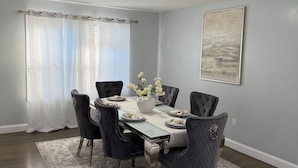 A dining room with a table set for six, six upholstered chairs, a vase with flowers, and a painting on the wall. - Rest in paradise, luxury and spacious home near NY (East Orange)