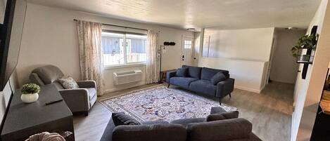 Ein modernes Wohnzimmer mit großem Teppich, zwei Sofas, einem Flachbildfernseher und einem Essbereich mit Tisch und Stühlen.