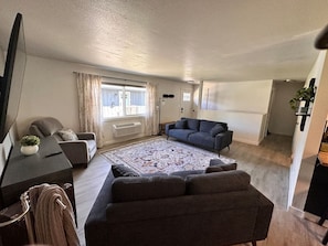Ein modernes Wohnzimmer mit großem Teppich, zwei Sofas, einem Flachbildfernseher und einem Essbereich mit Tisch und Stühlen.