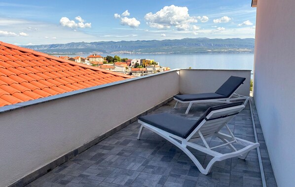 Ein Balkon mit zwei Liegestühlen, einem Ziegeldach und Blick auf einen See und Berge.