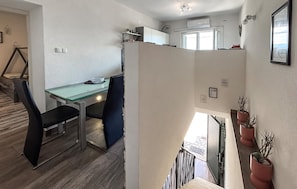 Eine moderne Küche mit weißen Schränken, einem Glastisch und Stühlen. Eine Treppe führt zu einer oberen Ebene mit einem Balkon.