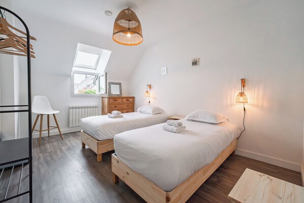 Un dormitorio con dos camas, un escritorio, una silla y una lámpara colgante.