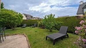 Ein Garten mit Rasen, zwei Liegestühlen, einem kleinen Gartenbeet und einer Hecke.