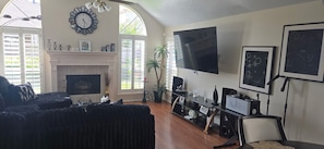 A living room with a fireplace, a large TV, and a sofa. - Beautiful 3-bedroom house w/AC in charming Cypress/Houston area. (Cypress)