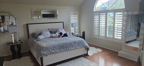A bedroom with a bed, a vanity with a mirror, a window with blinds, and a view of greenery outside. - Beautiful 3-bedroom house w/AC in charming Cypress/Houston area. (Cypress)