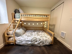 Ein Stockbett mit einer Leiter, einer Lichterkette und einem Kleiderschrank in einem Raum mit dunklem Boden.