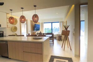 A modern kitchen with a central island, pendant lights, and a dining area with a view. - Luxury 2BR w/ Ocean Views • Gym • Jacuzzi • Infinity Pool • Walk Everywhere (Bucerías)