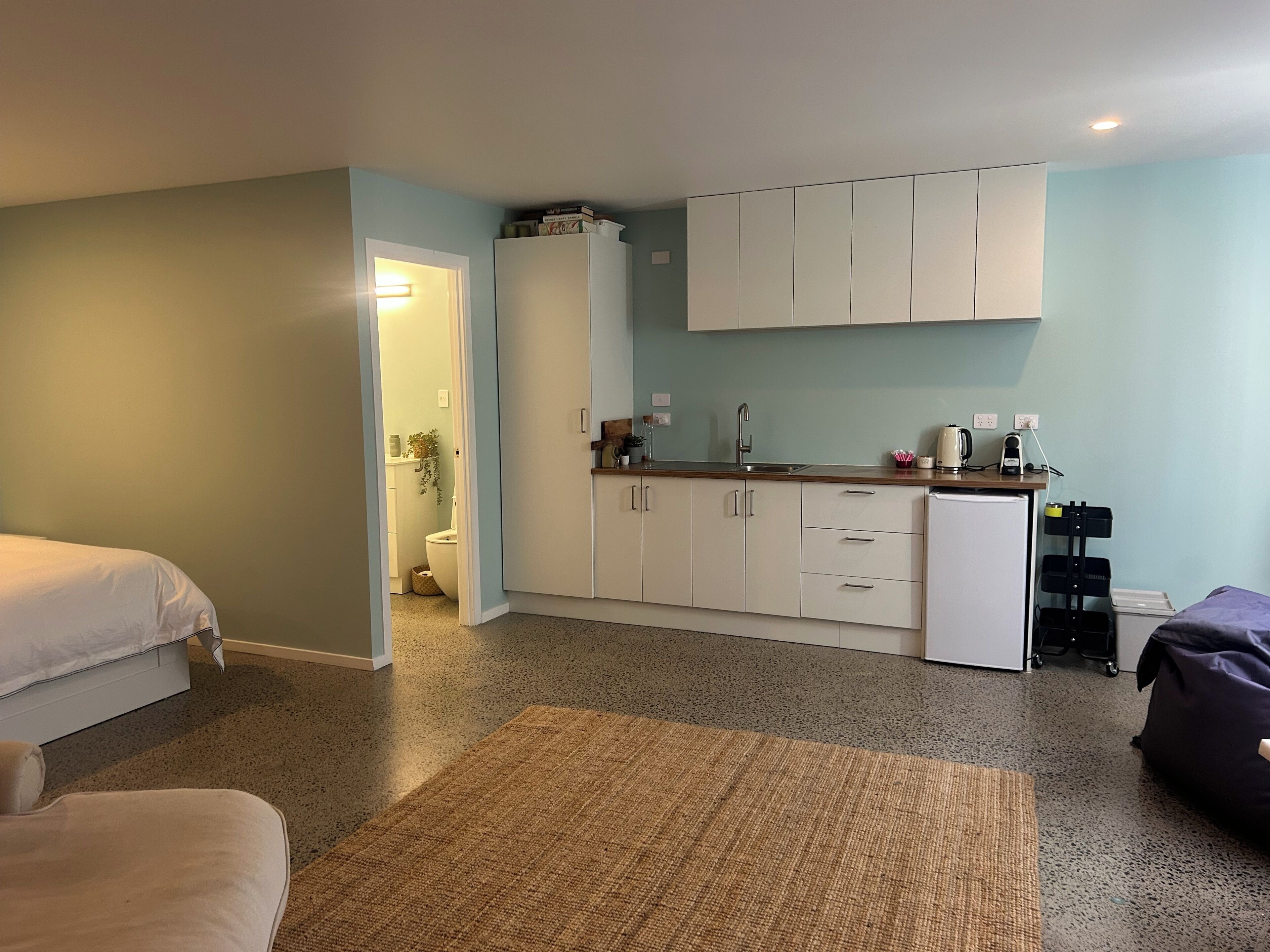 A compact room with a kitchenette, a bed, a small seating area, and a bathroom.