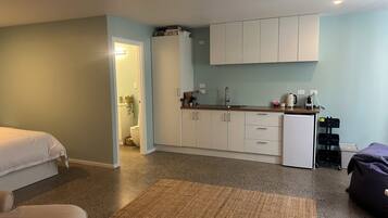 A compact room with a kitchenette, a bed, a small seating area, and a bathroom.