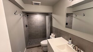 A bathroom with a shower, toilet, sink, and mirror.
