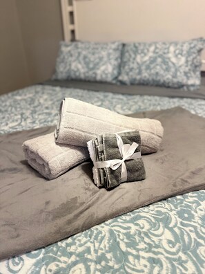Een bed met een beddegoed met een patroon, een grijze deken en twee opgevouwen handdoeken samengebonden met een lint.