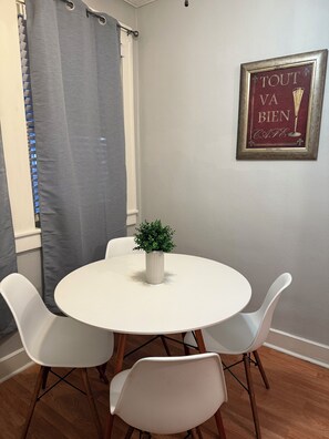 Een eetgedeelte met een ronde tafel, vier stoelen, een potplant en een lijst aan de muur.