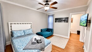 A bedroom with a bed, a blue sofa, a ceiling fan, a TV, and a painting on the wall.