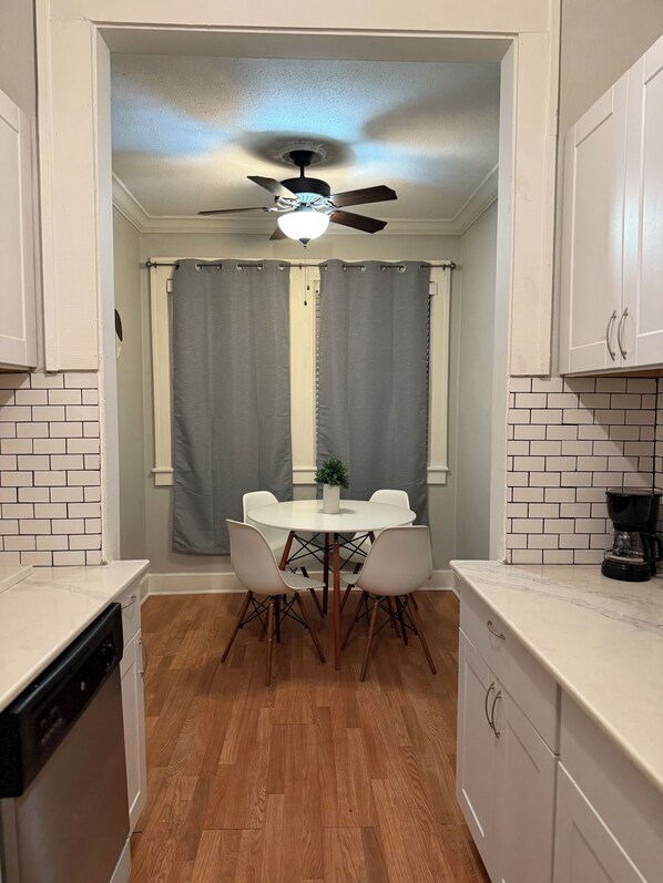 A compact kitchen with a dining table, chairs, a ceiling fan, and a coffee maker.