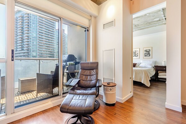 Una habitación con una silla de masajes, una cama, una pequeña mesa con un teclado y vistas a un edificio alto a través de una puerta de cristal.