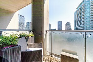 Ein Balkon mit Korbmöbeln, Blick auf Stadtgebäude und einen klaren Himmel.