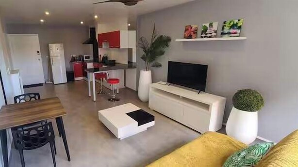 A compact living space with a dining area, kitchenette, and a seating area with a TV. - Appartement Fun et Agréable (papeete)