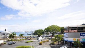A coastal cityscape with a marina, a large building with 'An' signage, and a clear sky. - Appartement Fun et Agréable (papeete)