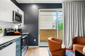 Une cuisine moderne équipée d’un four à micro-ondes, d’une cuisinière et d’un lave-vaisselle, une porte-fenêtre coulissante donnant sur un balcon et un fauteuil en cuir marron.