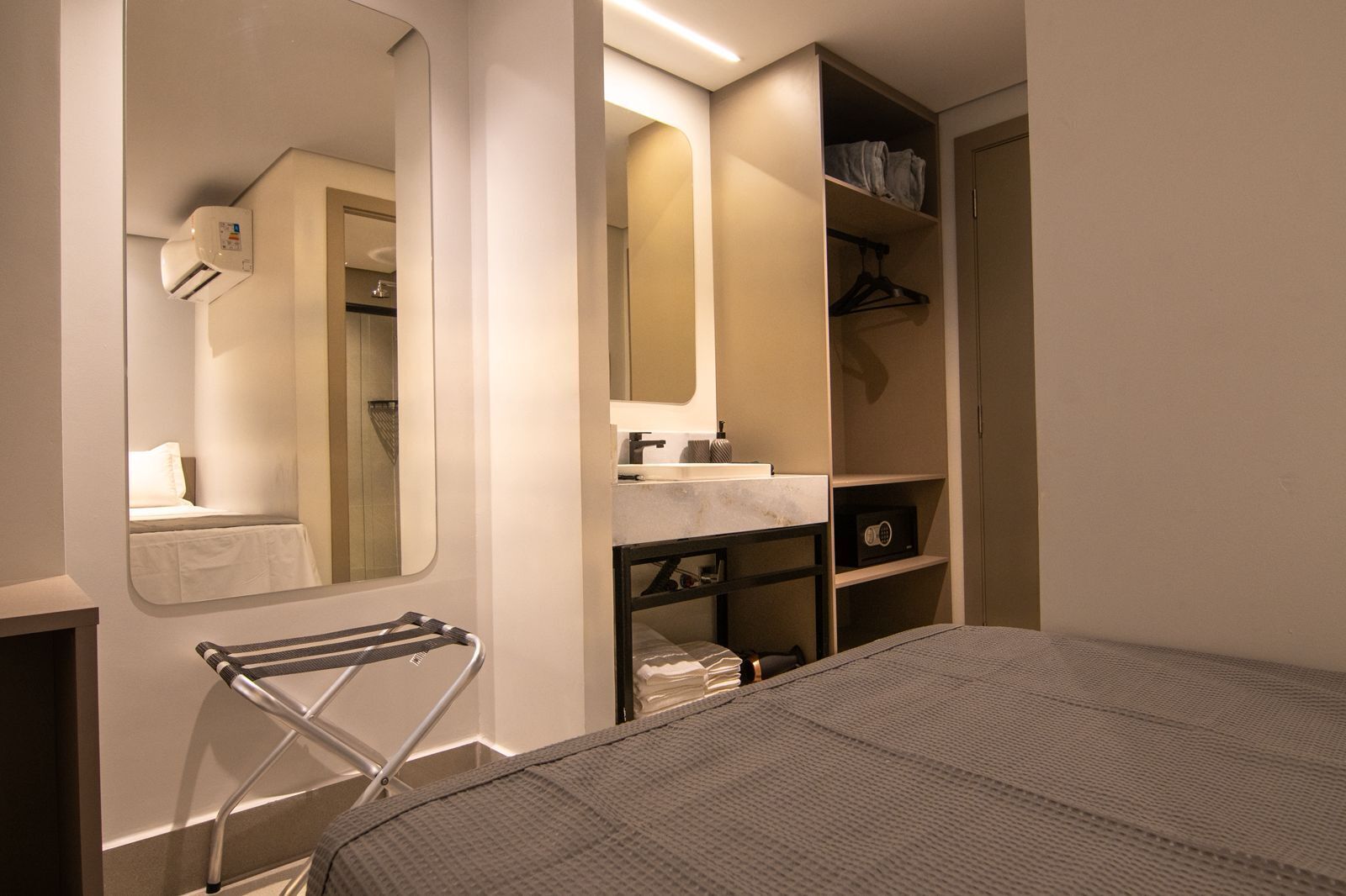 Hotellihuone, jossa on sänky, peili, pesualtaalla varustettu kylpyhuone ja vaatekaappi.