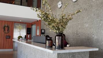 Un mostrador de recepción con un jarrón de flores, un reloj y un interior moderno con techos altos y vistas al piso superior.