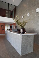 Un mostrador de recepción con un jarrón de flores, un reloj y un interior moderno con techos altos y vistas al piso superior.