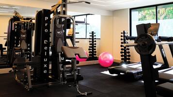 Un gimnasio con varios equipos de ejercicio, incluyendo una banca de pesas, una jaula para sentadillas y una cinta de correr.
