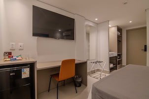 A hotel room with a bed, a desk, a chair, a TV, a mirror, and a wardrobe.