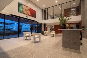 A lobby with a reception desk, seating area, and a large window overlooking a parking area. - Hotel Mandu (Teresina)