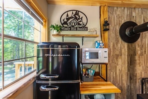 Eine Küche mit einem schwarzen Kühlschrank, einer Mikrowelle, einem Holzregal mit einer Pflanze und einem Schild mit der Aufschrift 'Windy Hill Bunkie'.